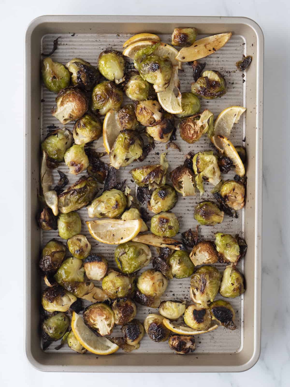 A sheet pan with brussels sprouts that have been roasted for 30 minutes, topped with lemon wedges whose juice has been squeezed into the brussels sprouts.