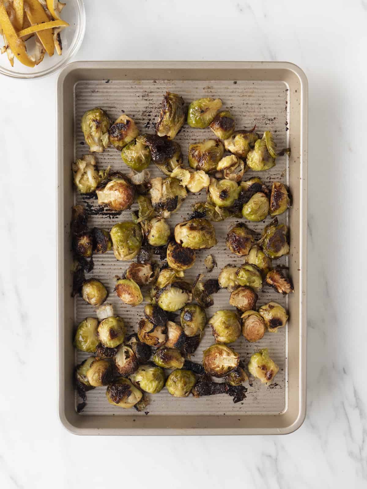 A sheet pan with crispy lemon brussels sprouts and a small mixing bowl of lemon wedges that have been picked out when the dish completed cooking.