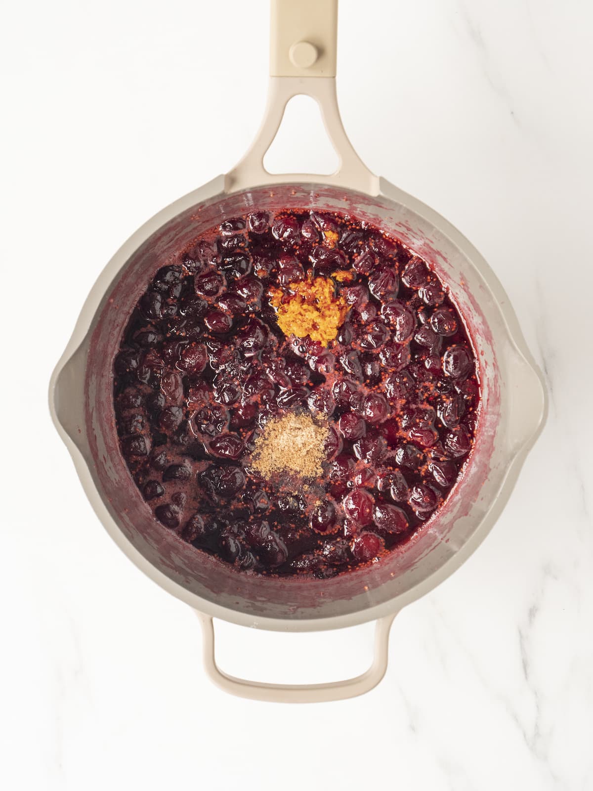 White medium saucepan with cooked cranberries in water and sugar topped with nutmeg and orange zest.