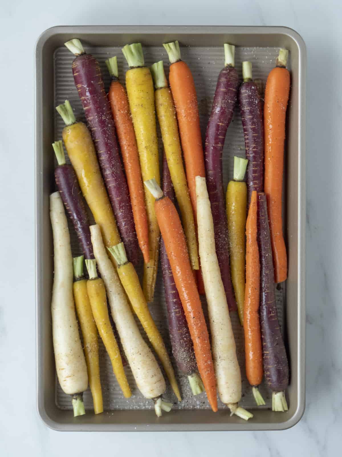 A sheet pan with heirloom carrots drizzled with olive oil, and a sprinkle of salt, pepper and red pepper flakes.