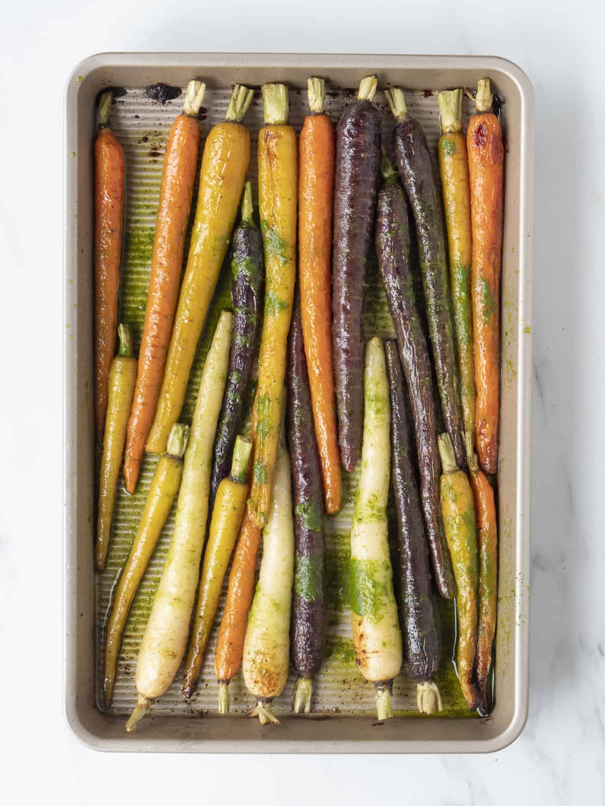A sheet pan with roasted heirloom carrots drizzled with vinaigrette.