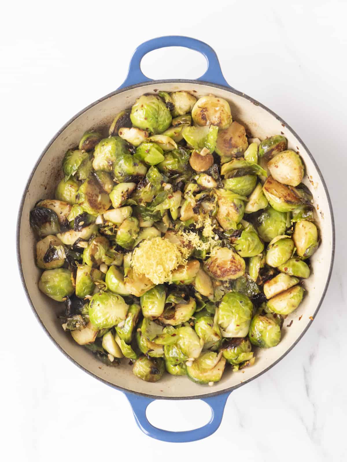 Large blue dutch oven with sautéed brussels sprouts topped with lemon zest.