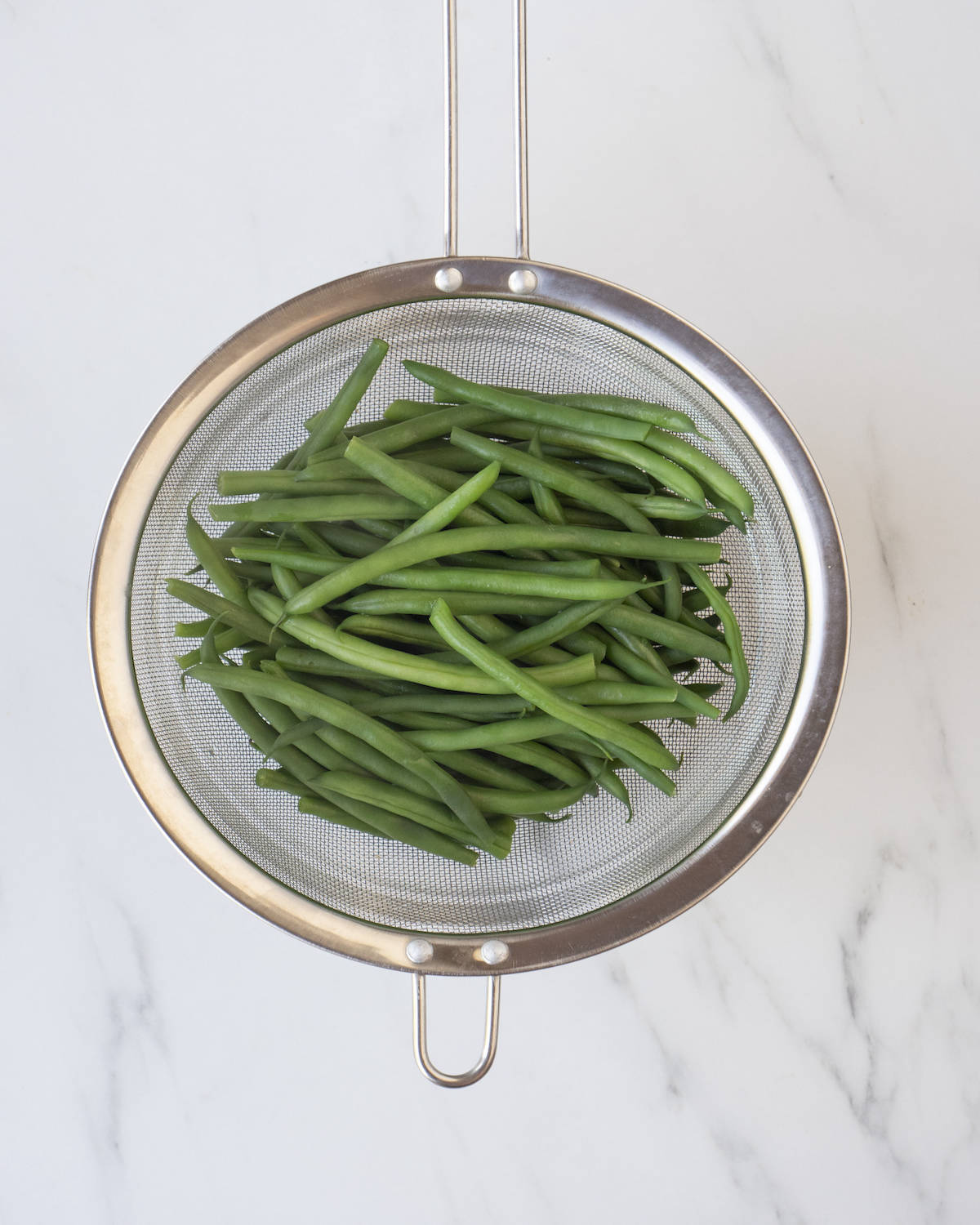 Green beans in a mesh metal strainer on a white countertop.