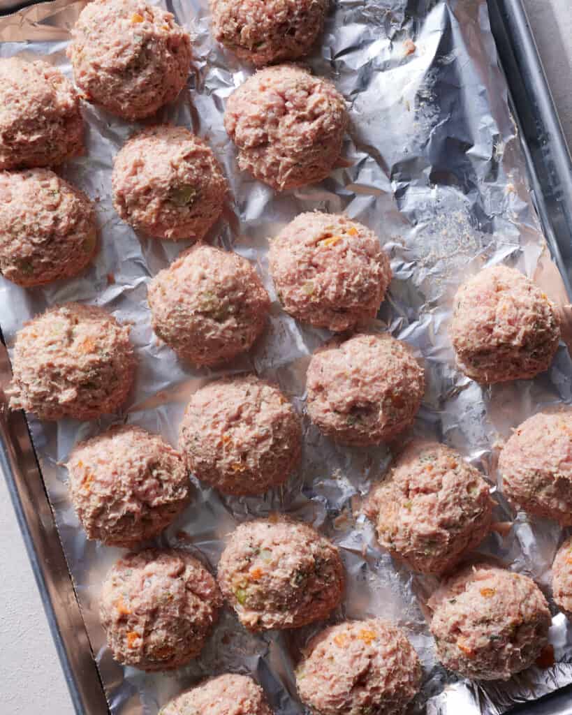 A baking sheet lined with aluminum foil with raw turkey meatballs on it.