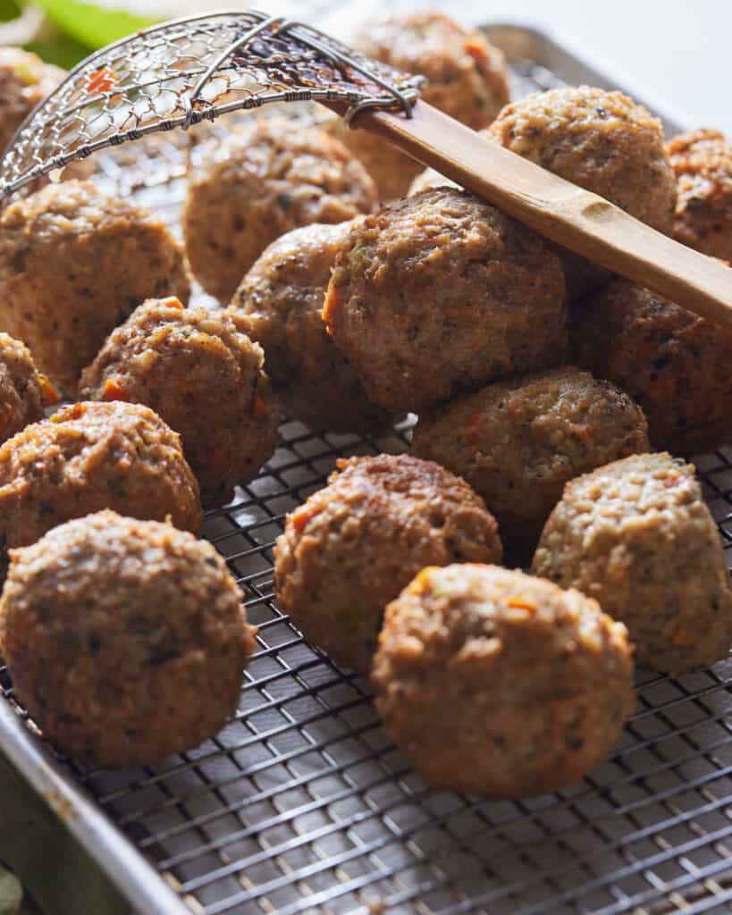 A baking sheet with a wire rack and fried turkey meatballs and a spider strainer spoon on them.