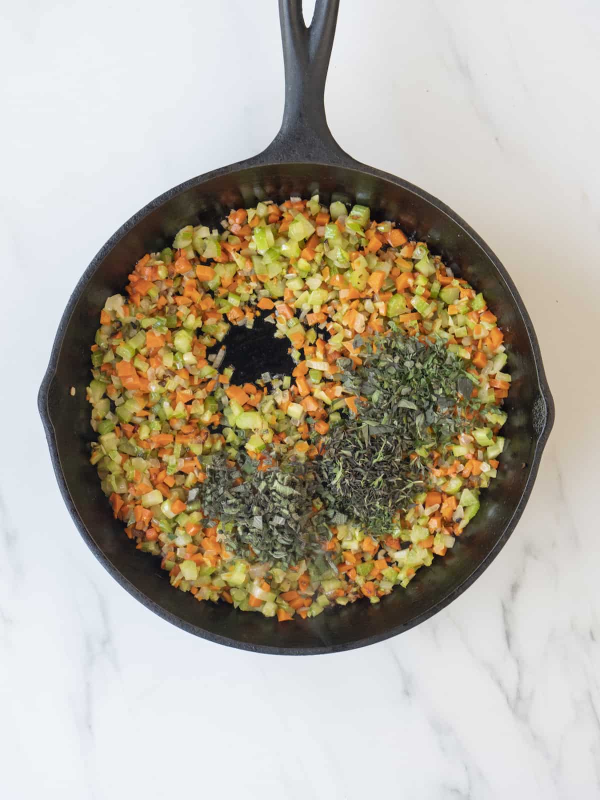 A skillet with chopped vegetables being cooked and topped with freshly chopped sage, thyme and oregano.