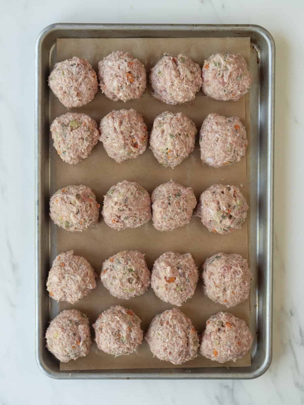 A baking sheet lined with parchment paper, with raw turkey meatballs on it in a 5x4 grid.