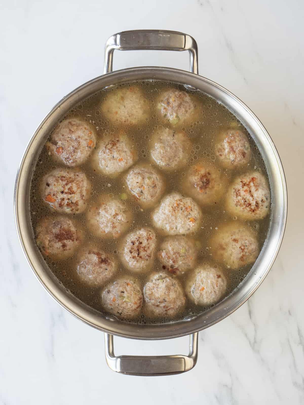 A large saucepan with stock and fried meatballs in it, completed submerged.