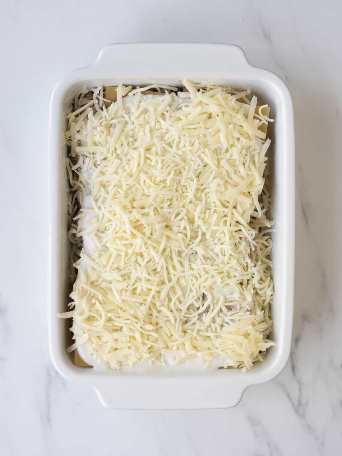 A white rectangular baking dish with uncooked lasagna assembled.