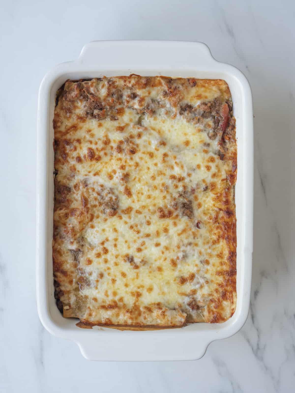 A white rectangular baking dish with lasagna baked with a browned cheesy top.