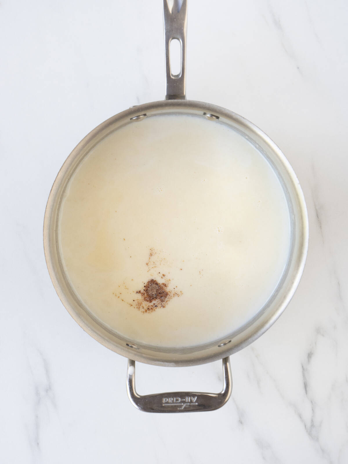 A saucepan with roux to make béchamel sauce with milk just poured in and nutmeg sprinkled on top.