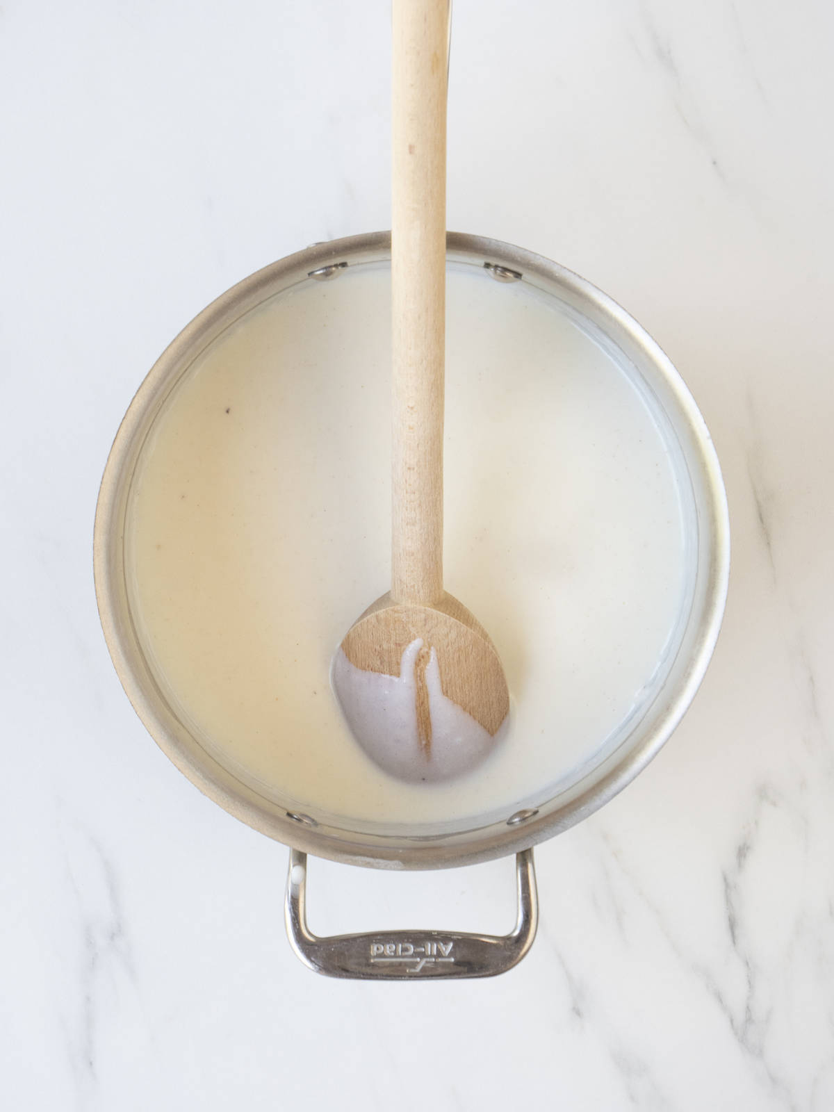 A saucepan with béchamel sauce with a wooden spoon.