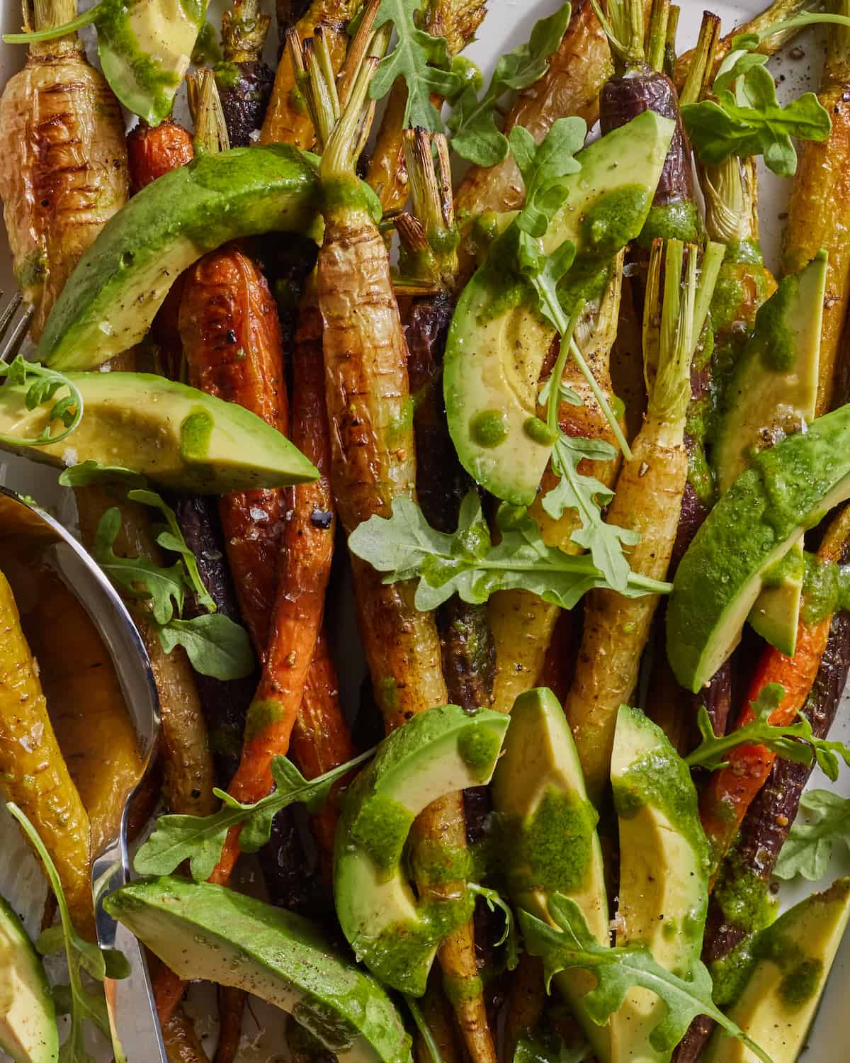 A close-up shot of roasted carrots drizzled with vinaigrette, and topped with arugula and avocado.