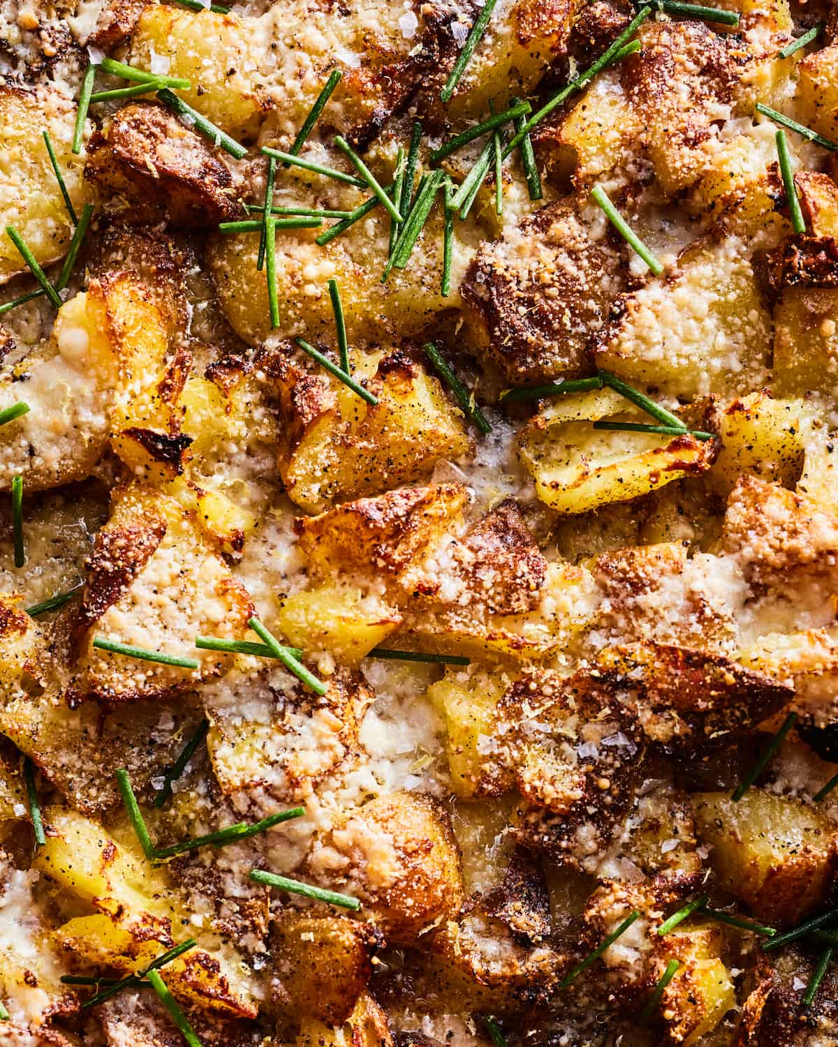 An overhead tight shot of cubed golden crispy roasted potatoes with melted parmesan cheese and chives