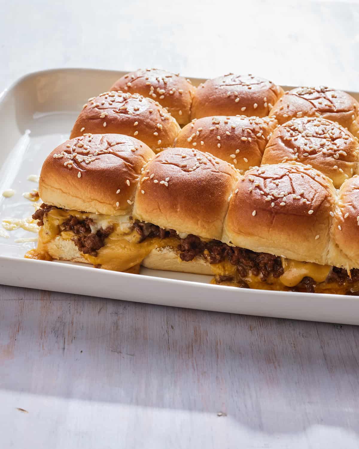 A white platter with a grid of cheeseburger sliders.