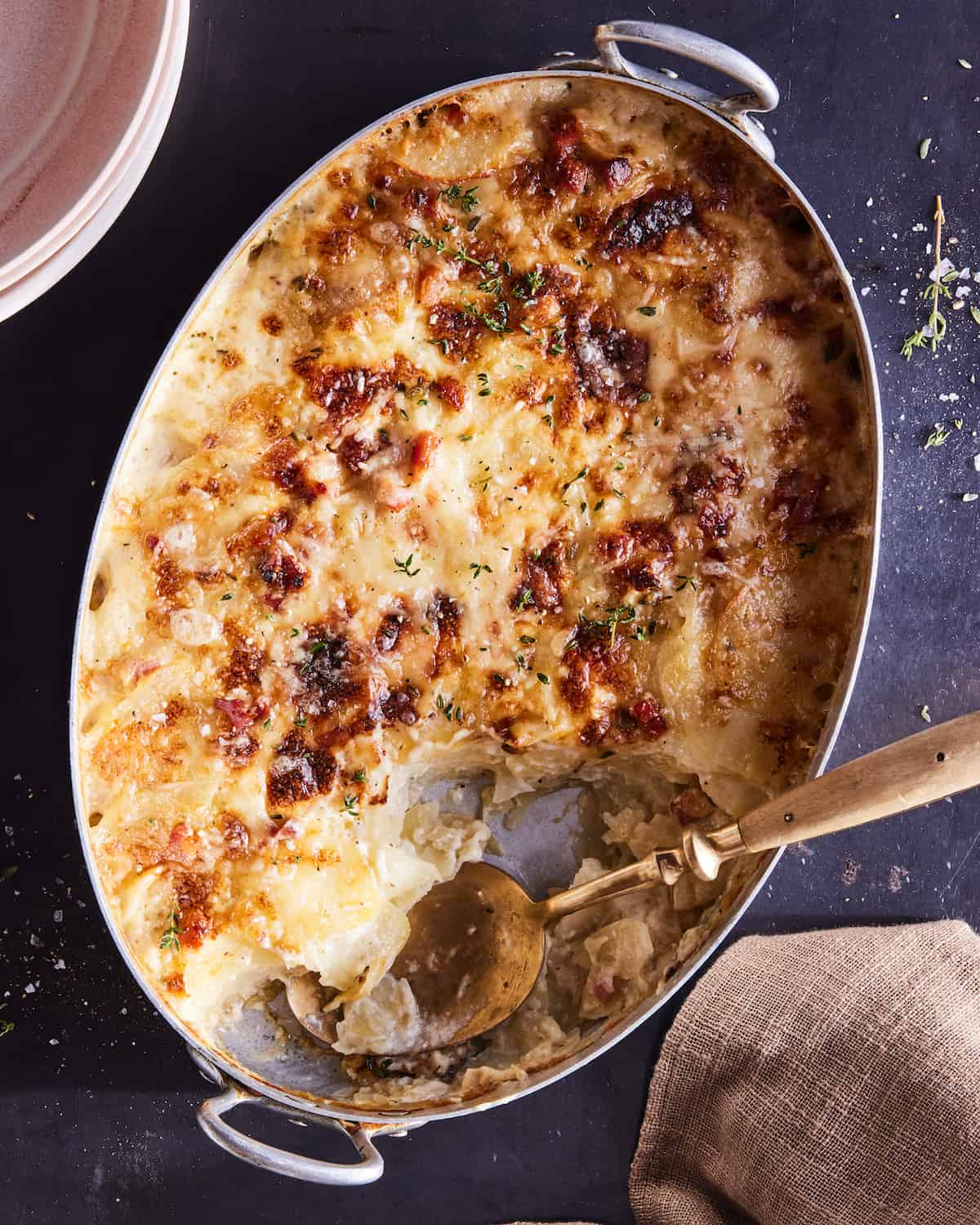 An oval dish with potatoes au gratin with some servings taken out, and a serving spoon.