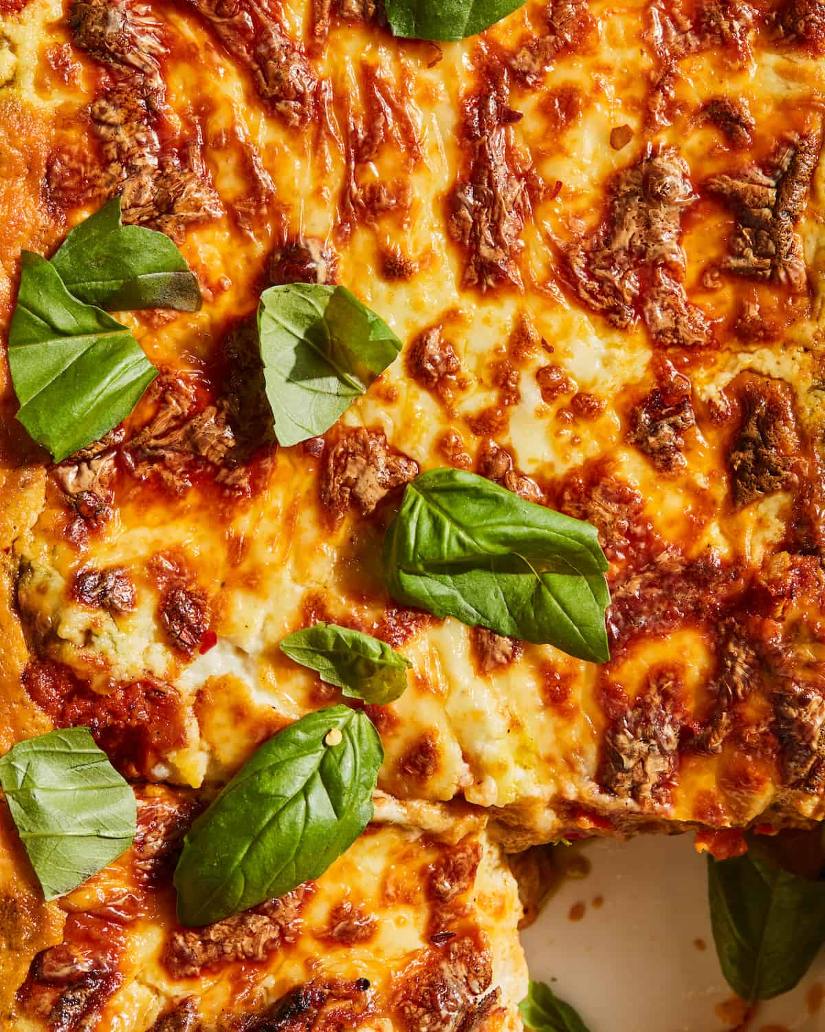 A close-up shot of three meat lasagna, garnished with basil leaves.