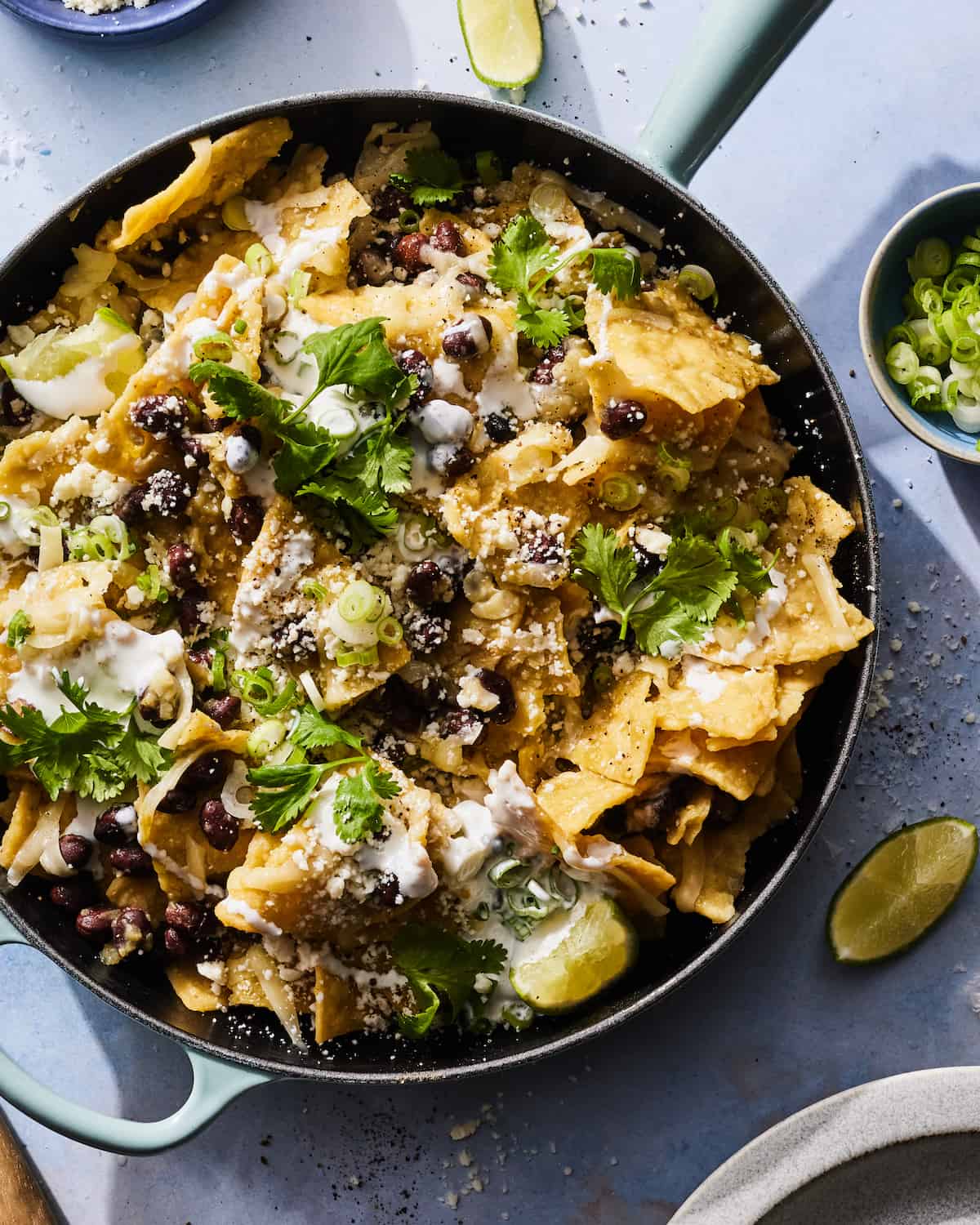 A large skillet with Chilaquiles next to a sliced lime and some sea salt sprinkled on the table.  