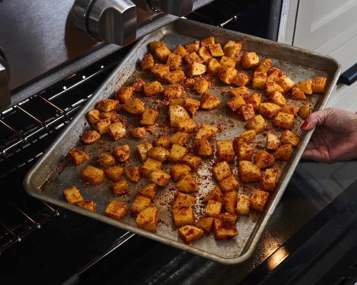 A woman placing a baking sheet with cubed potatoes into an oven.