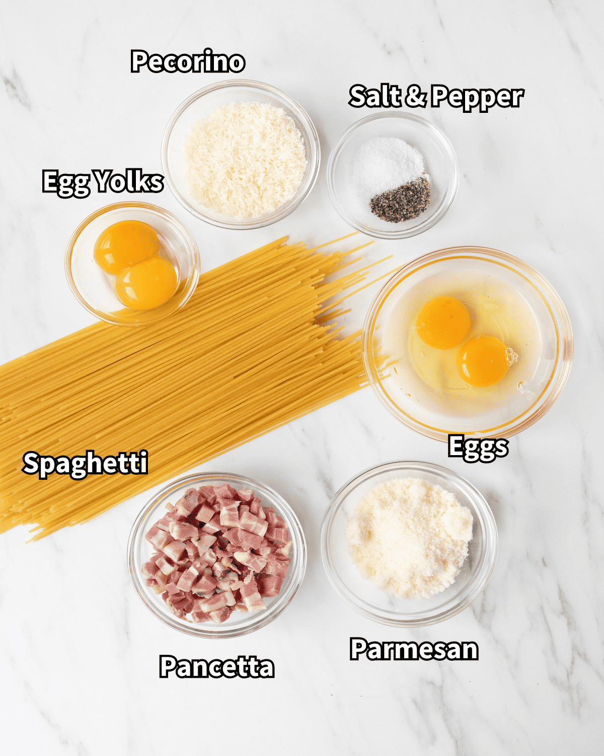 Ingredient shot of clear bowls with individual ingredients for the Spaghetti Carbonara including pancetta, eggs, spaghetti, parmesan, pecorino, salt and pepper, and egg yolks.
