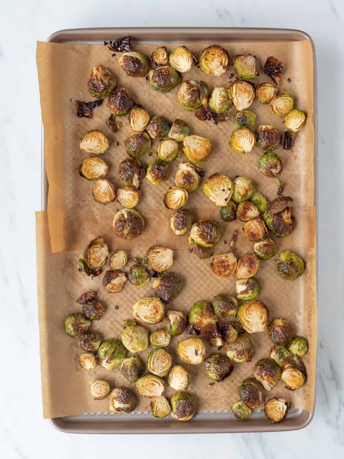 A baking sheet pan lined with parchment paper with halved roasted brussels sprouts.