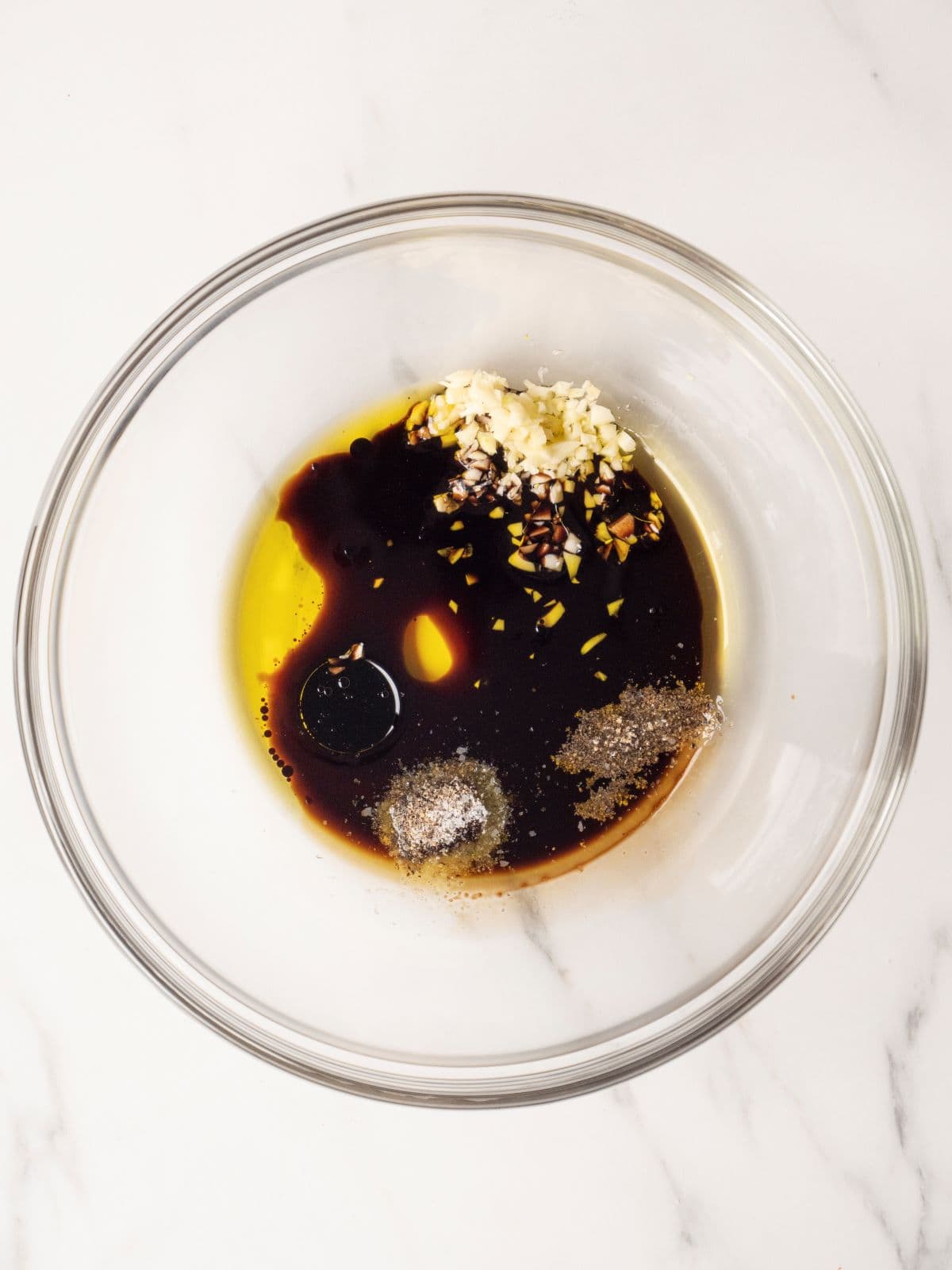 A small glass mixing bowl with a mix of olive oil, balsamic vinegar, garlic, salt and pepper.