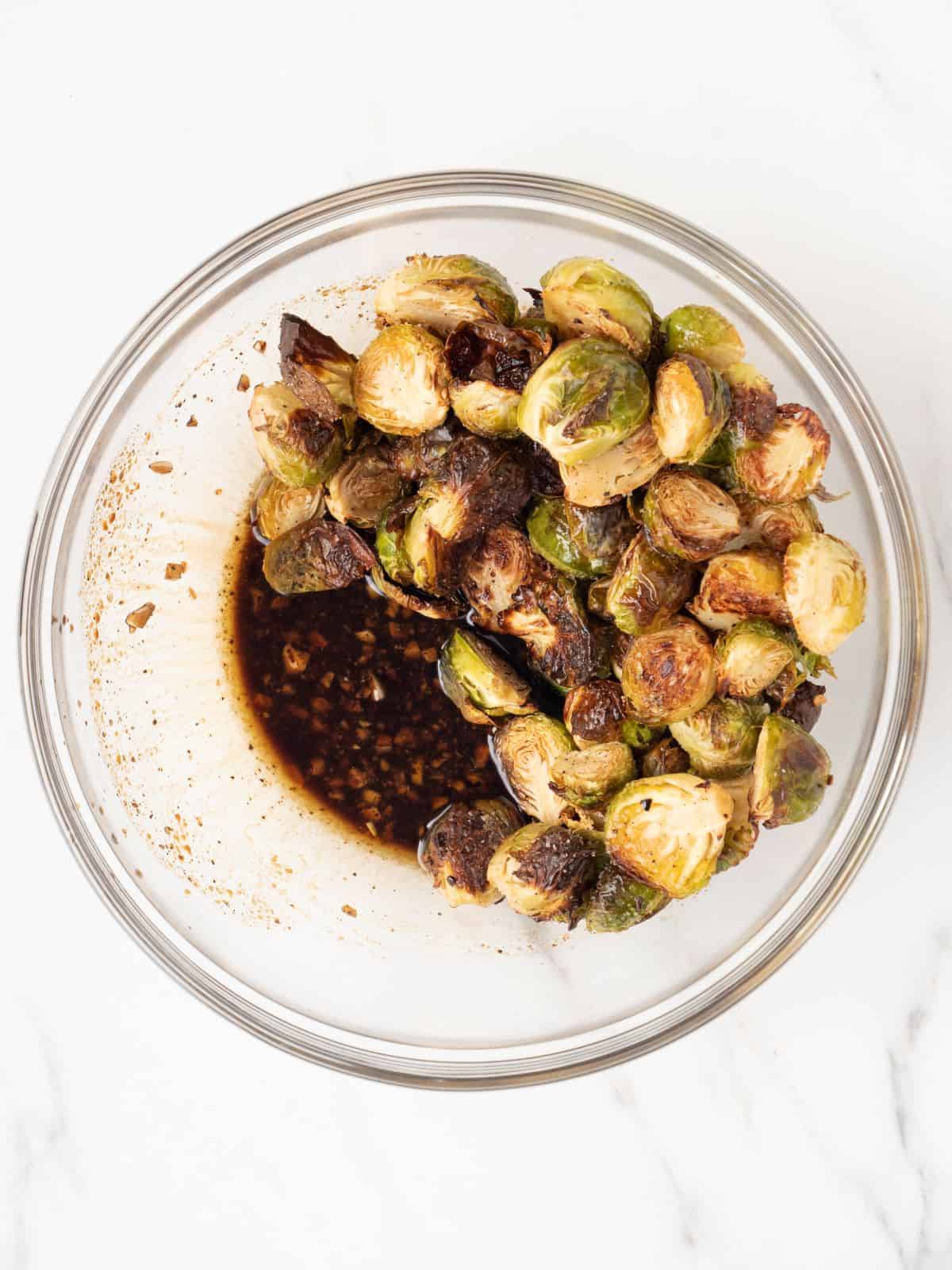 A small glass mixing bowl with roasted brussels sprouts added to the dressing.