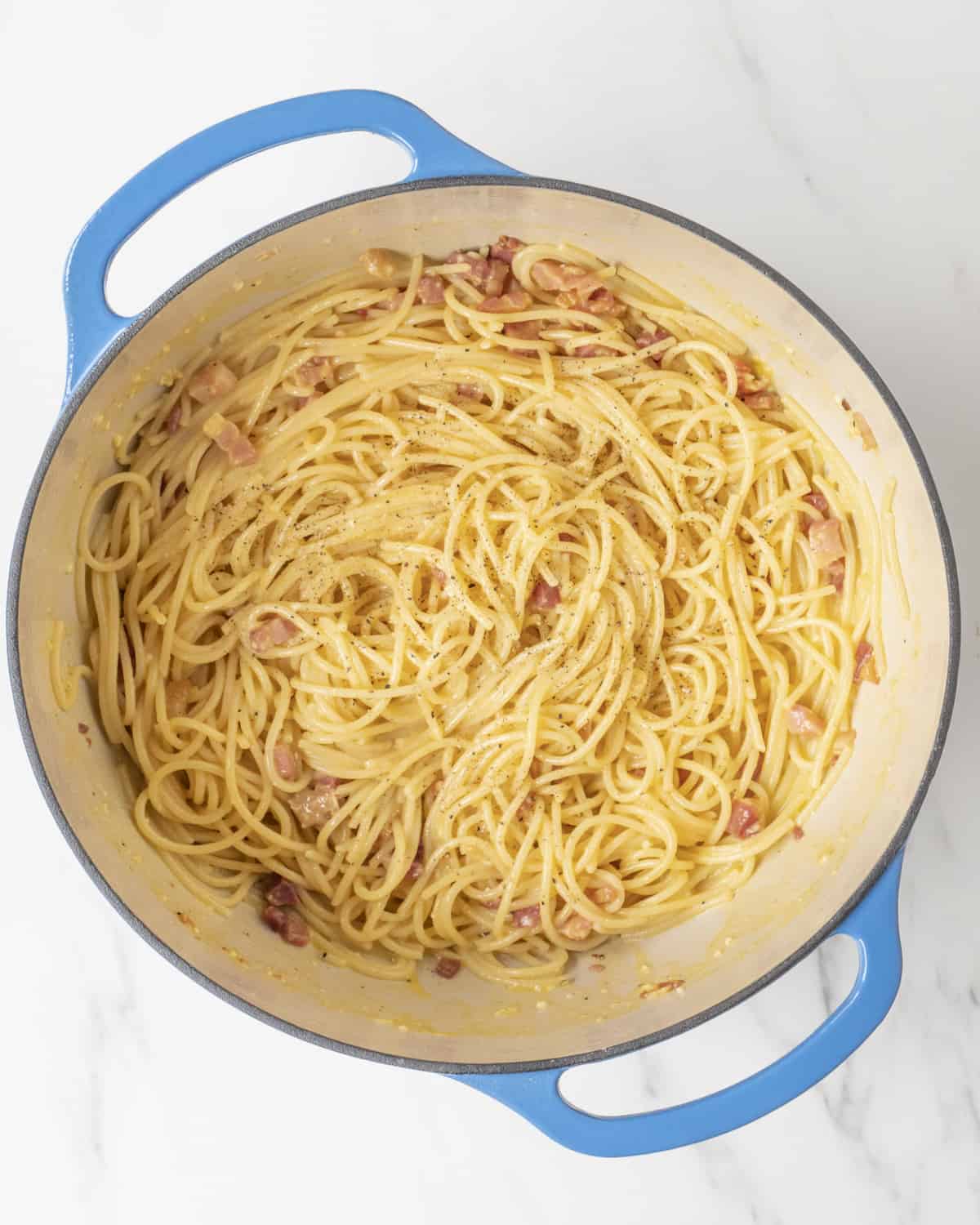 A blue Dutch oven skillet with the completed Spaghetti Carbonara recipe.