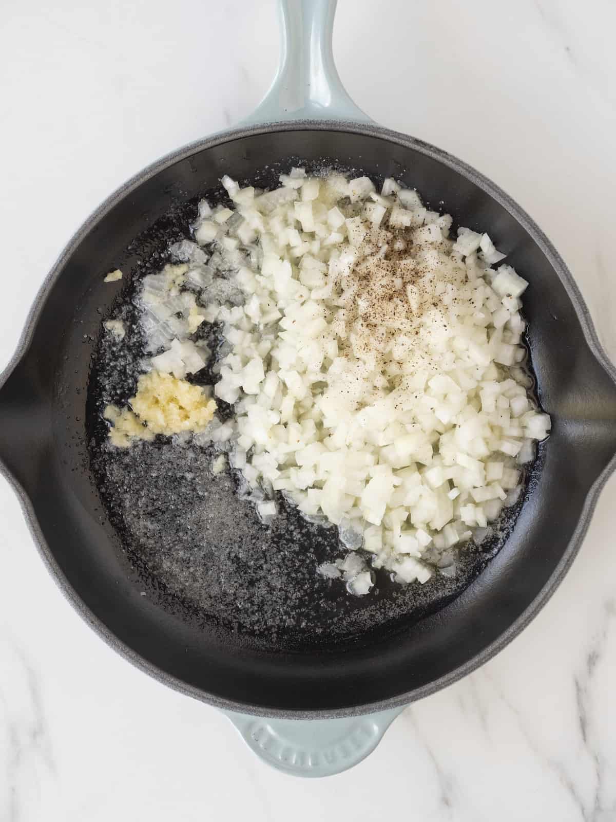 A skillet with butter and some chooped onion and garlic along with salt and pepper.