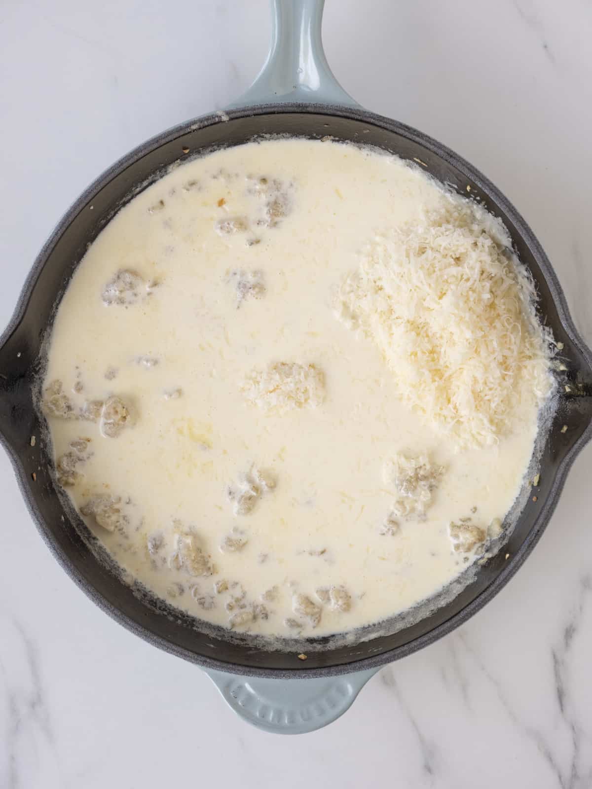 A skillet with an onion and roux base with cream and grated parmesan just added.