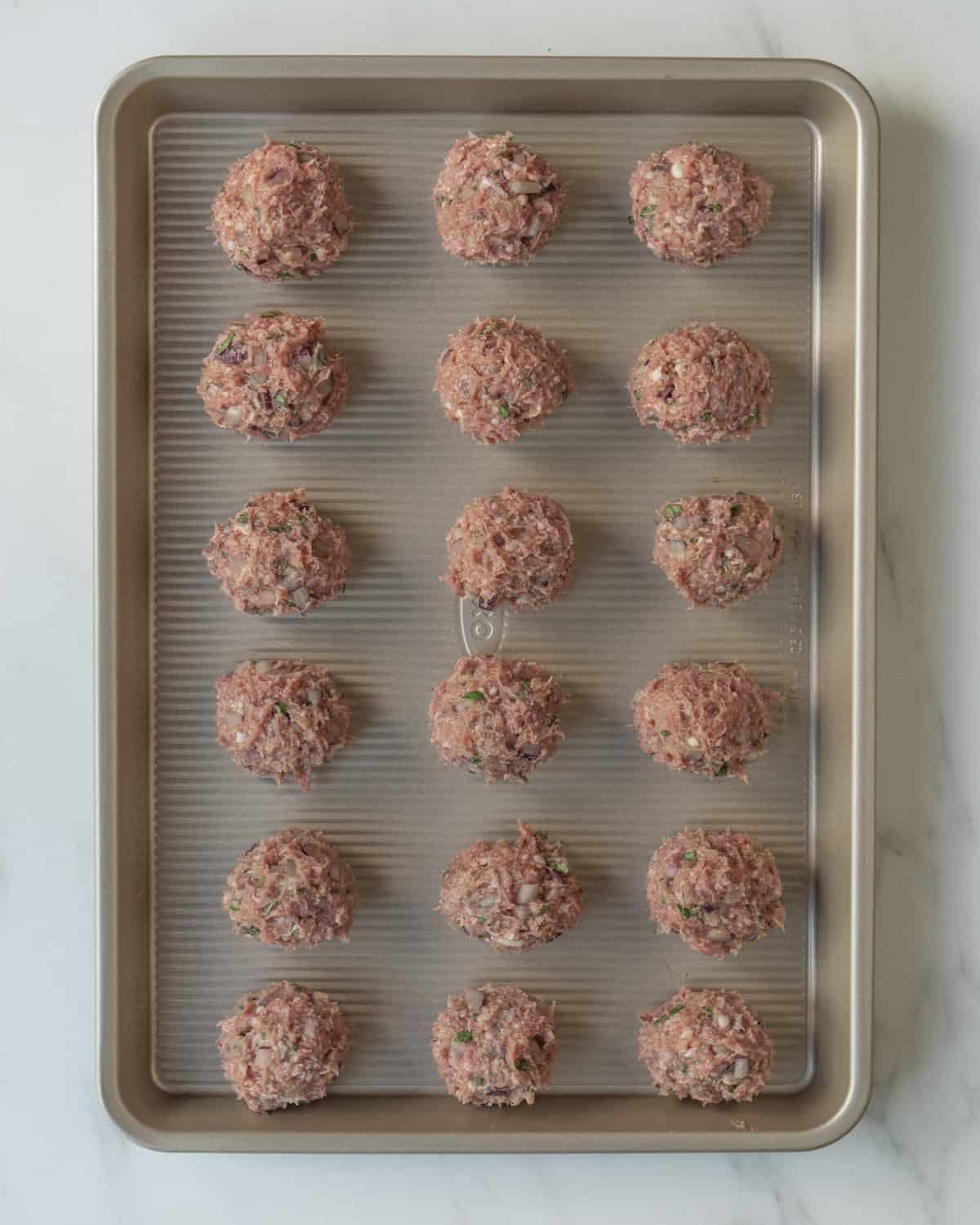Uncooked meatballs lined on a metal sheet pan.
