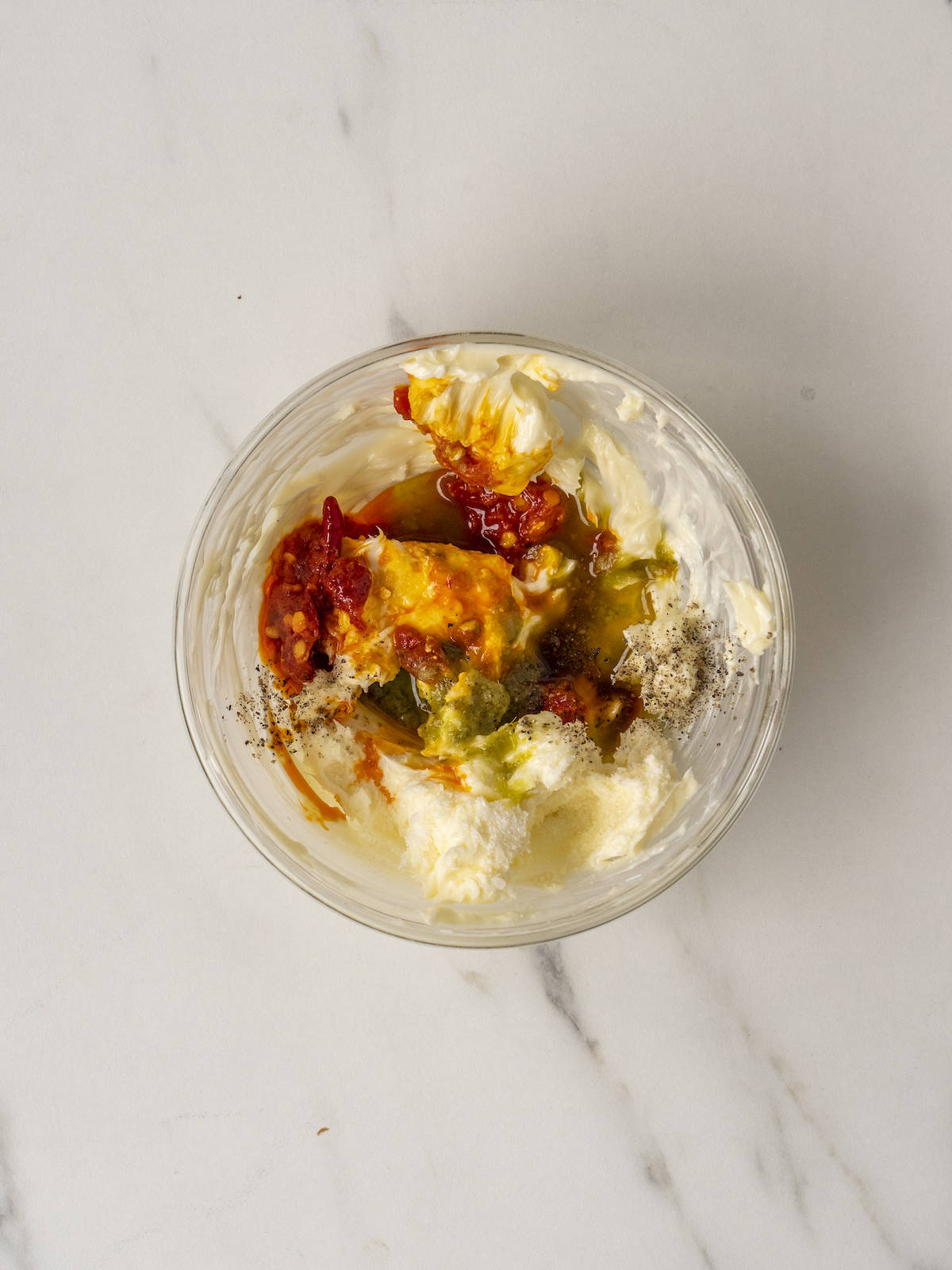 A small glass mixing bowl with butter, calabrian chiles, basil vinaigrette and salt and pepper.