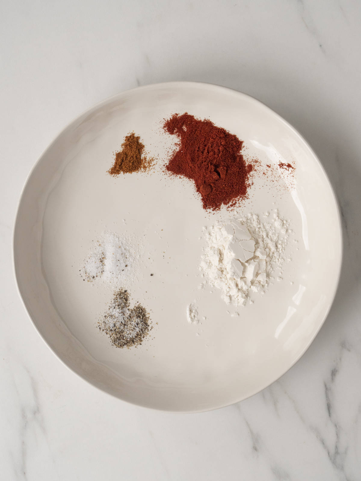 A white low bowl with flour, paprika, cayenne pepper and salt and pepper.