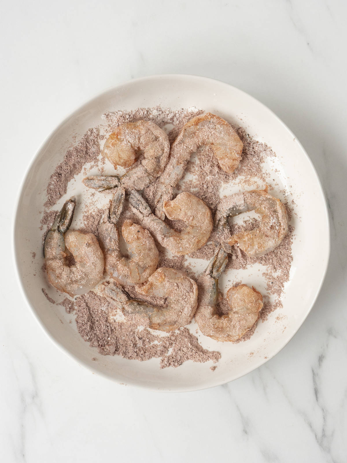 A white low bowl with shrimp coated with a flour and spice mixture.