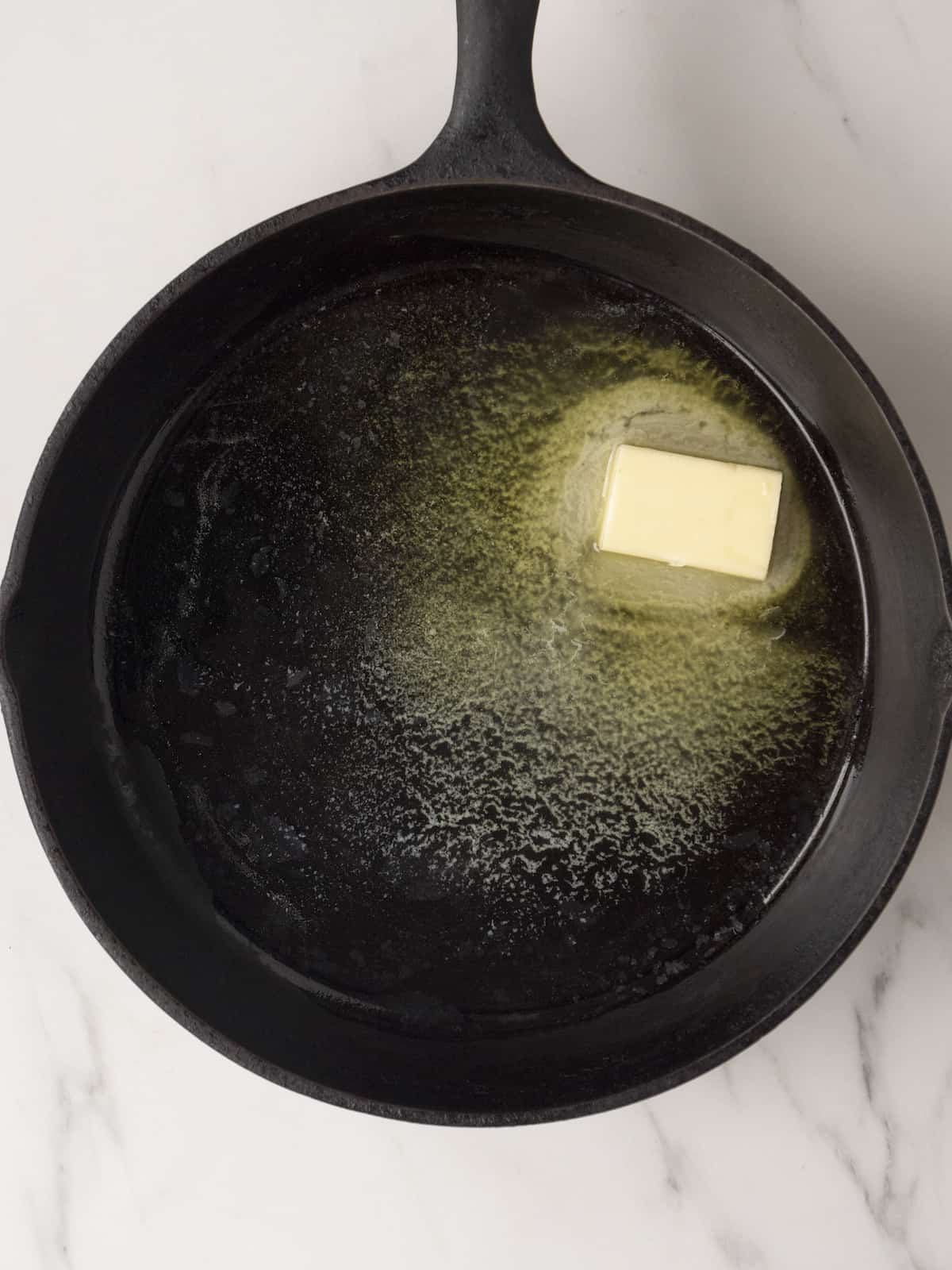 A skillet with olive oil and a piece of butter partially melting.