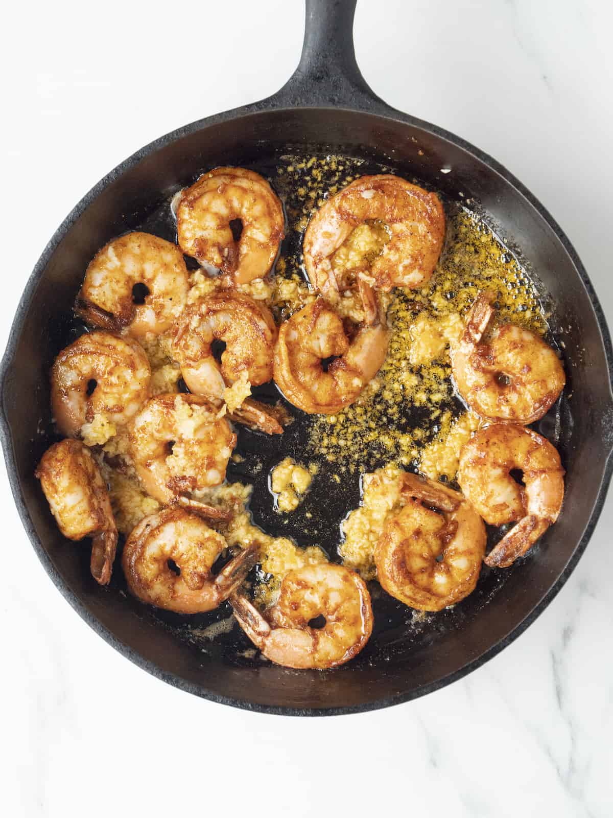 A skillet with Hawaiian garlic shrimp in a chili butter sauce with minced garlic added.