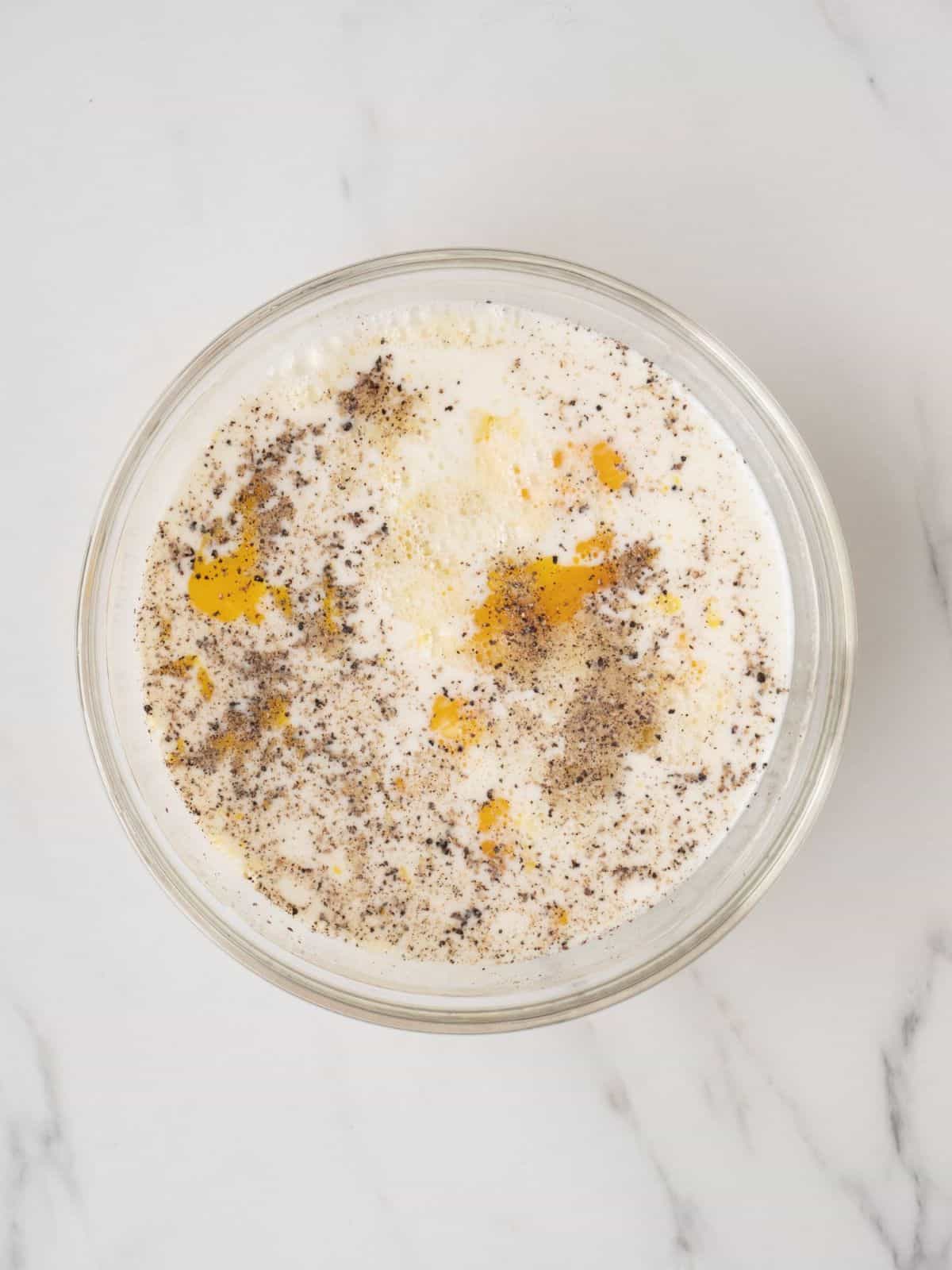A glass mixing bowl with eggs, milk, salt and pepper mixed together.