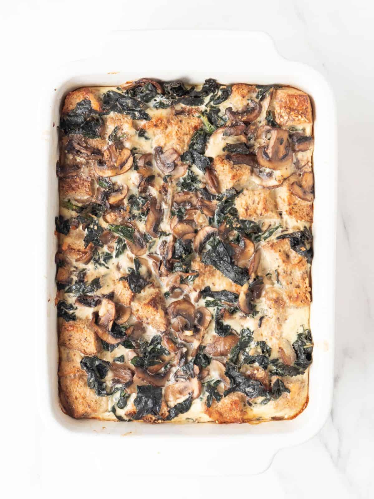 A white rectangular baking dish with freshly baked kale and mushroom bread pudding.