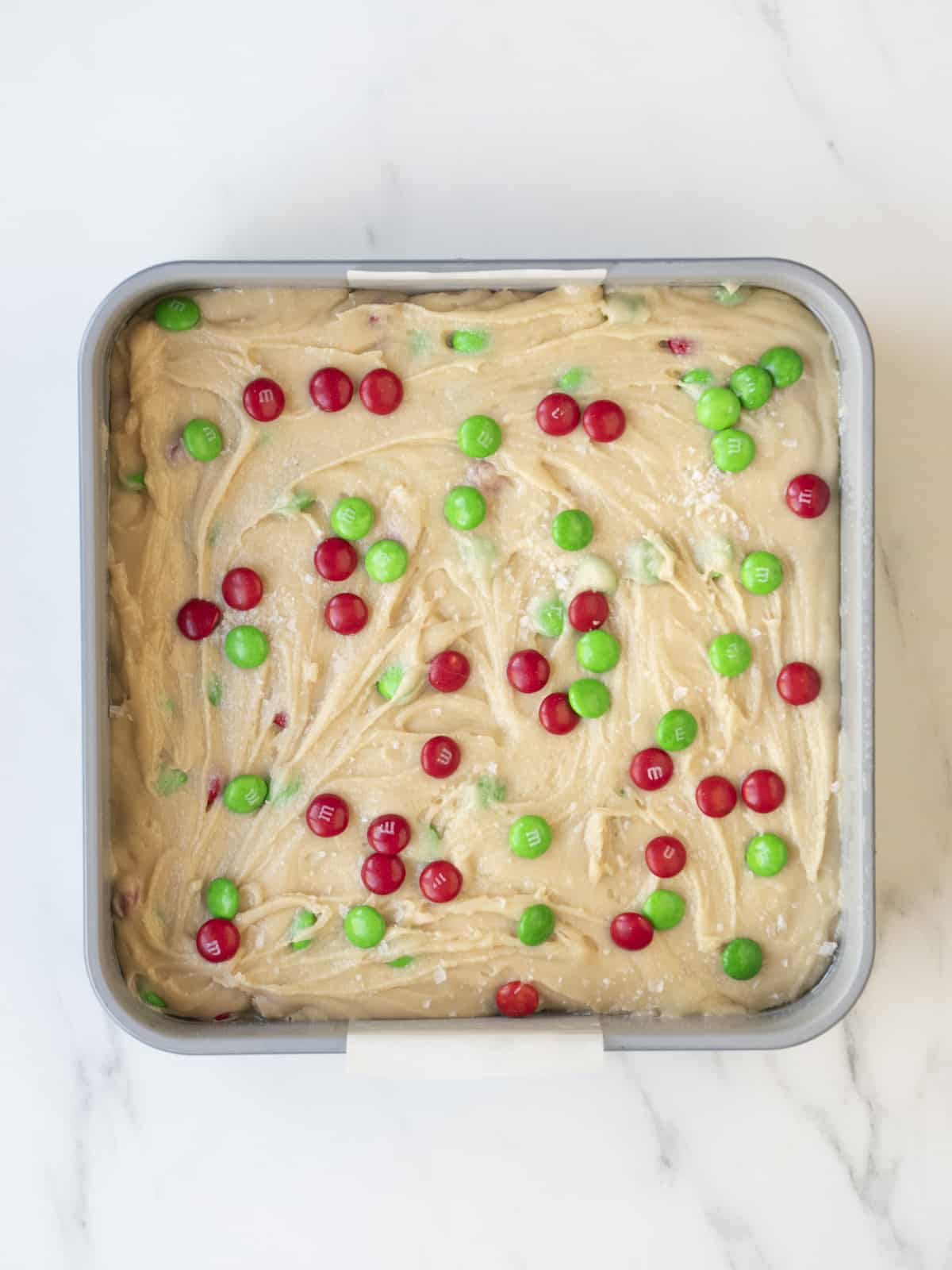 A square baking pan with M&M cookie batter and topped with red and green M&Ms.