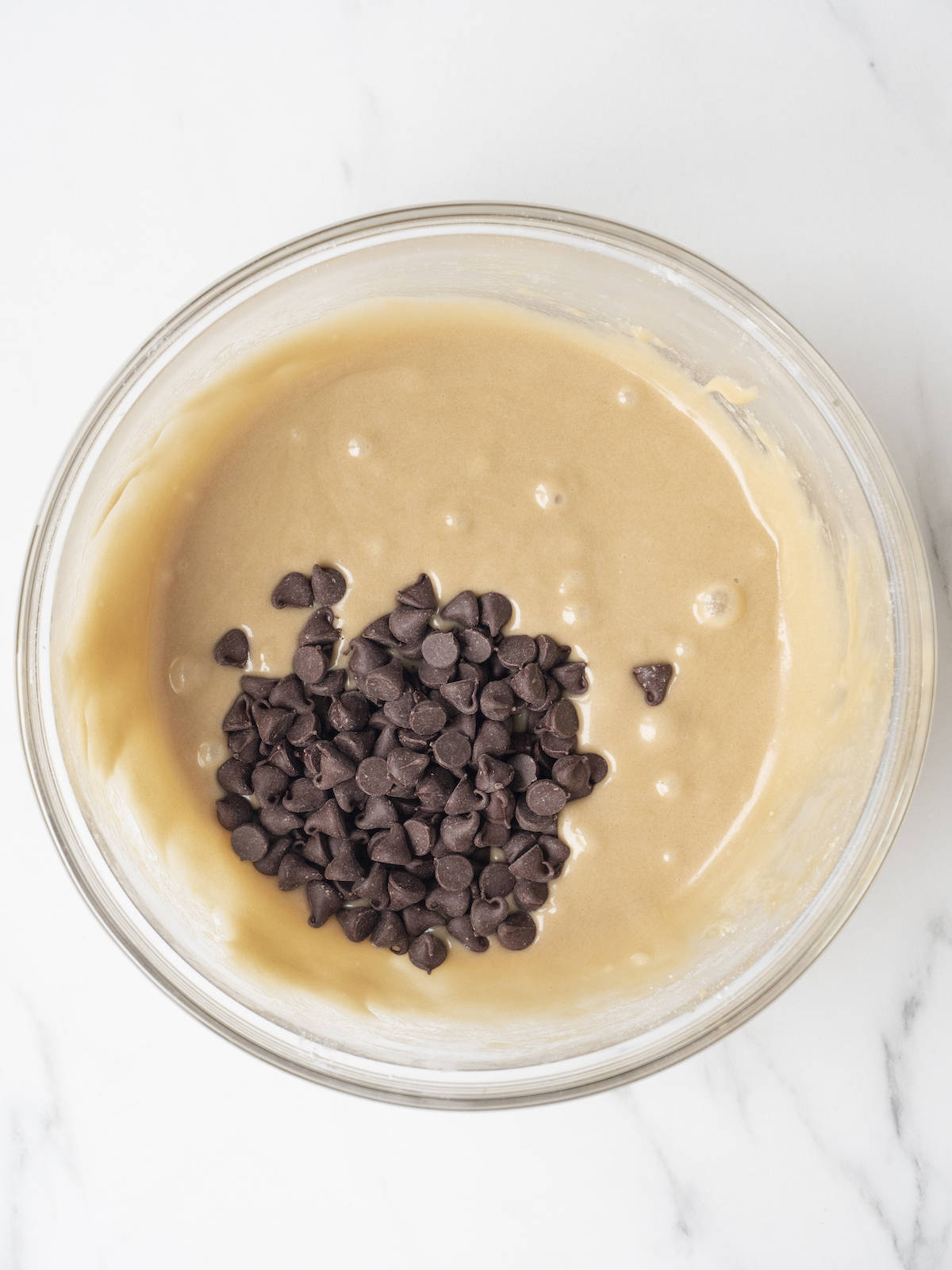 A glass mixing bowl with cookie dough batter with chocolate chips added.