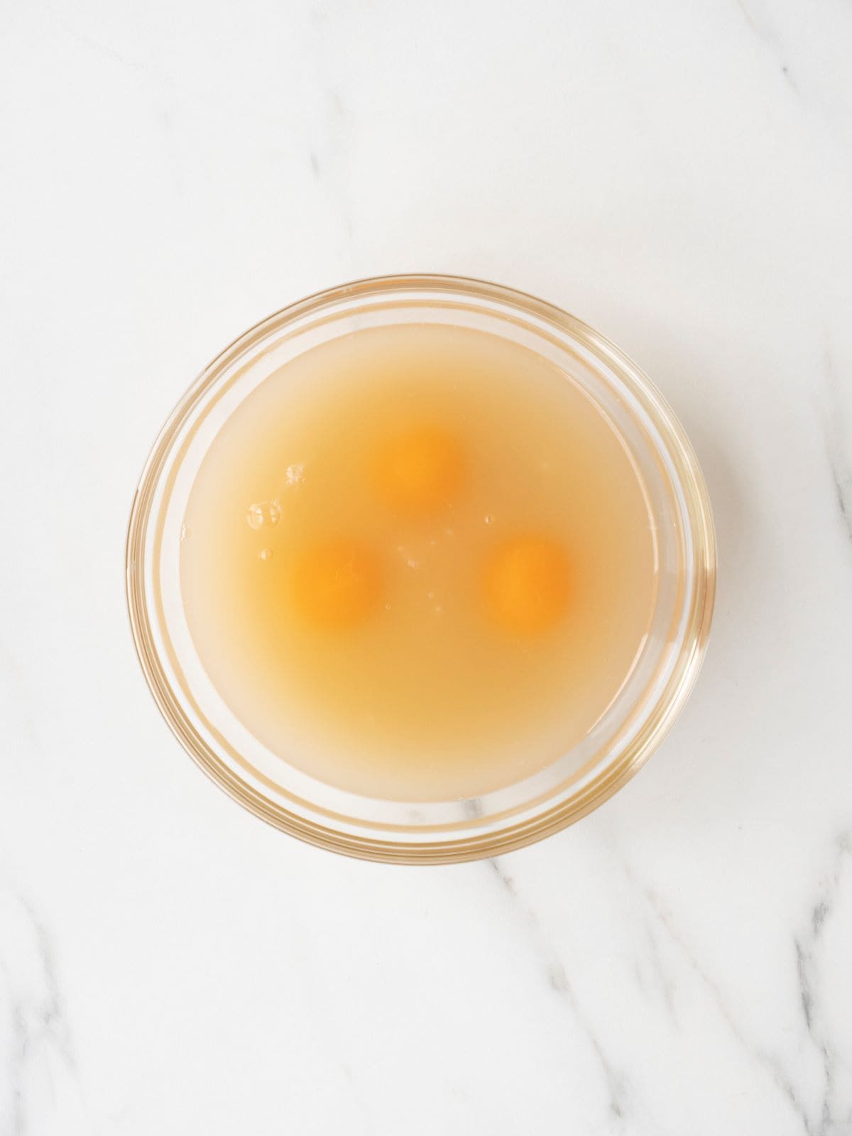 A small glass mixing bowl with eggs and chicken broth.
