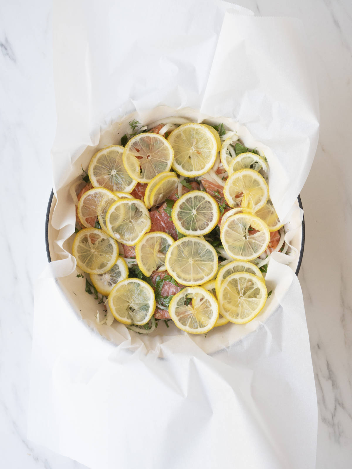 A skillet lined with parchment paper with the salmon fillets completely covered with thin slices of lemon.