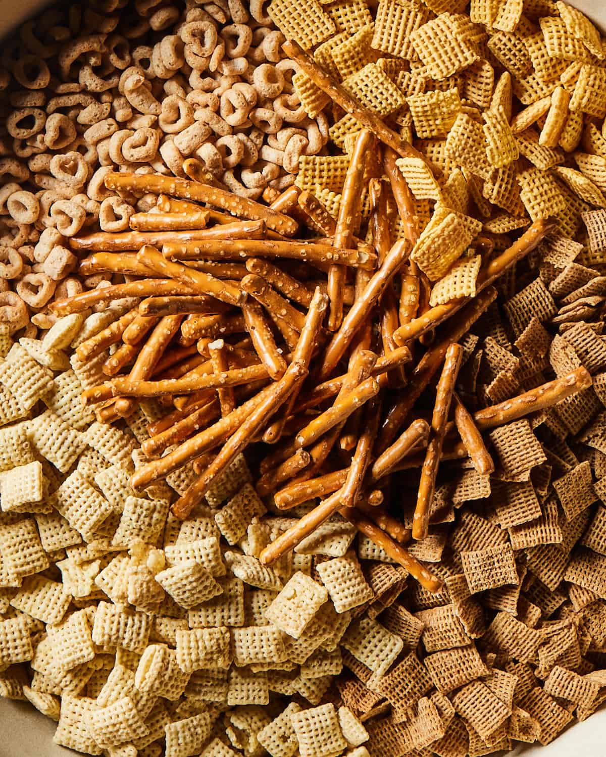 A close-up shot of corn chex, wheat chex, rice chex, cheerios and pretzel sticks laid out.
