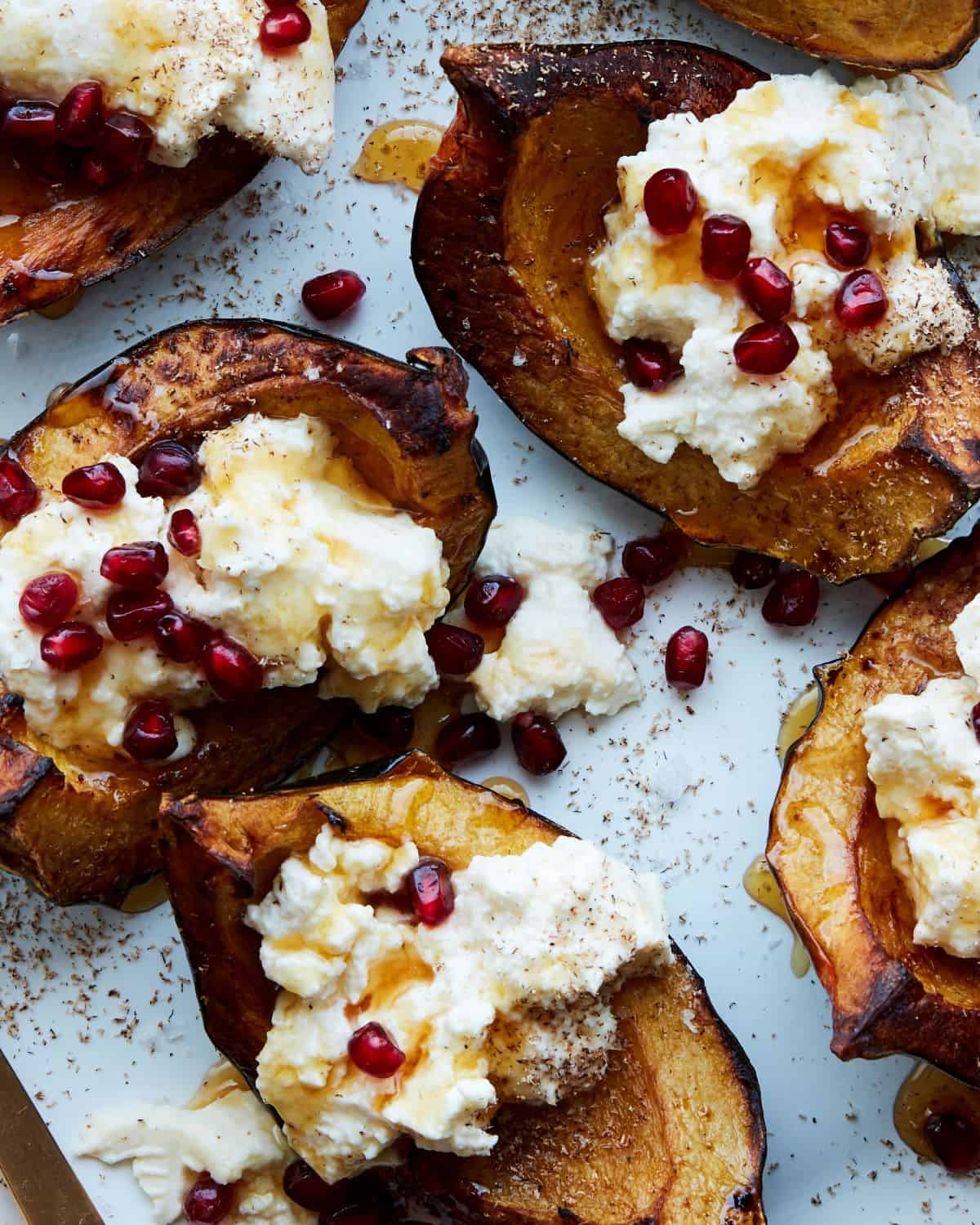 A close-up shot of roasted acorn squash, topped with ricotta, pomegranate seeds, and honey and nutmeg.