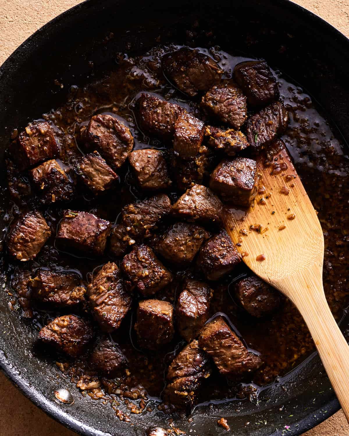 Garlic Butter Steak Bites in a cast iron skillet with a wooden spoon on a wooden countertop.
