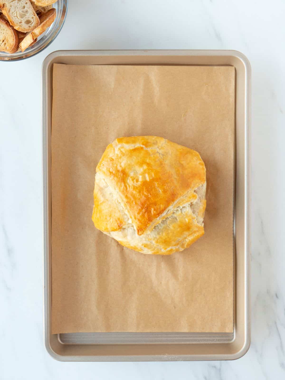 A parchment-lined sheet pan with brie wrapped in puff pastry baked and of out the oven