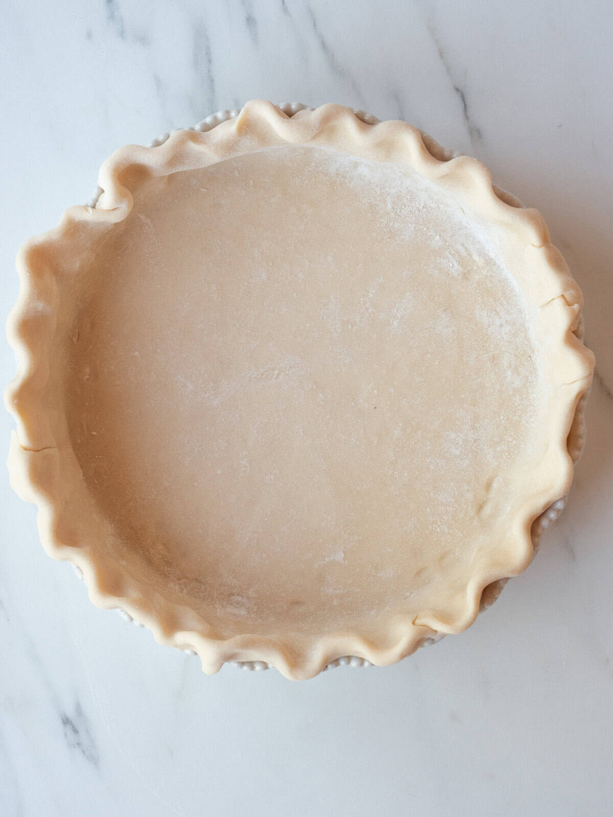 A pie dish with pie dough rolled out into it with the edges crimped.