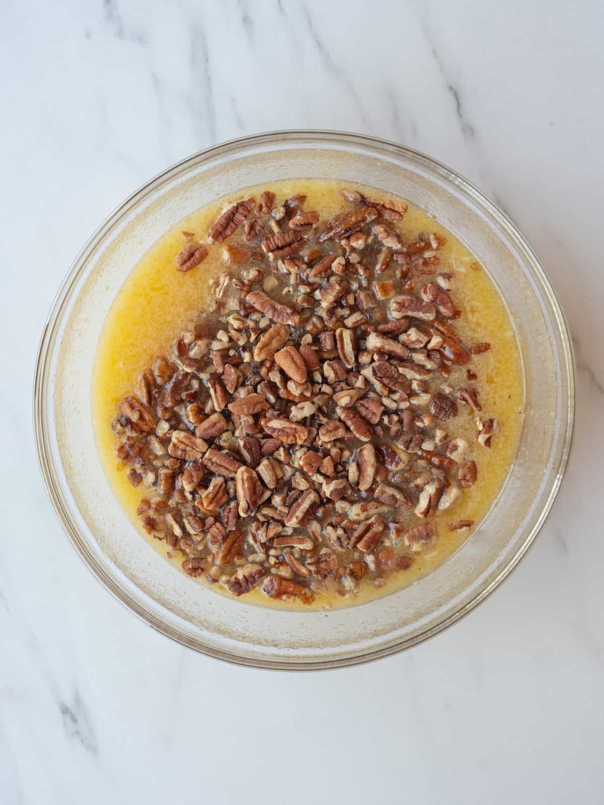 A mixing bowl with wet ingredients for pecan pie mixed together and pecans folded in.