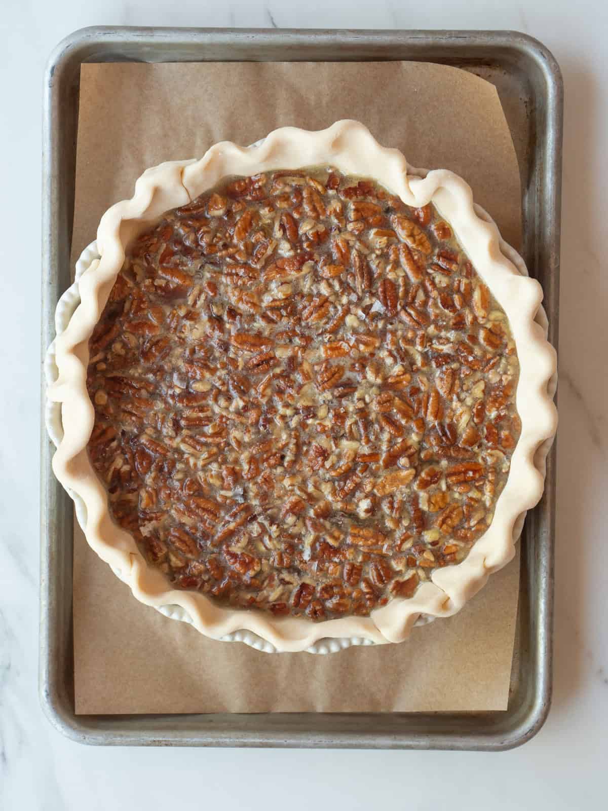 A baking sheet with a pie dish placed on it, with a brown butter bourbon pecan pie ready to be baked in the oven.