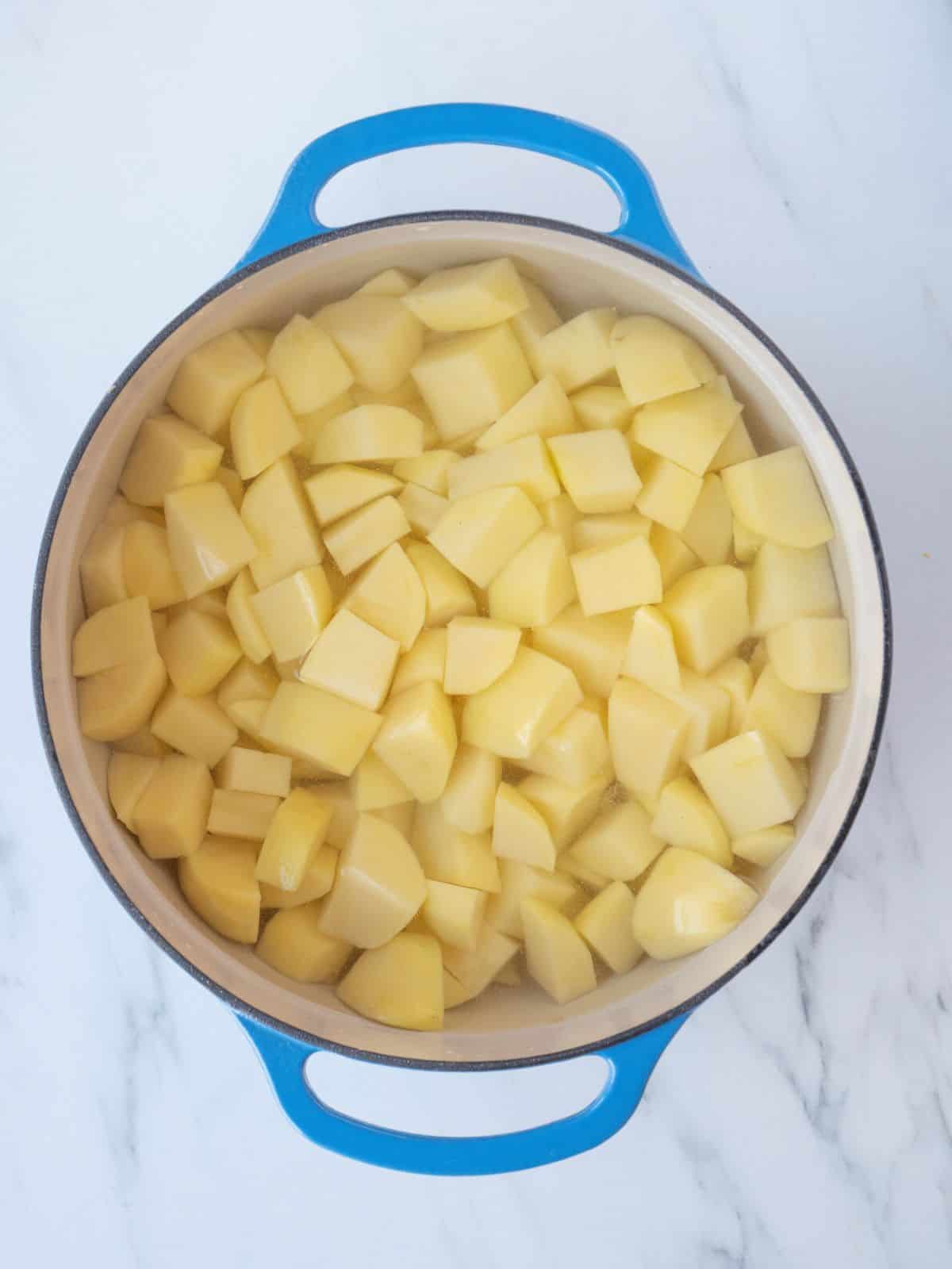 A blue dutch oven with cubed potatoes in water.
